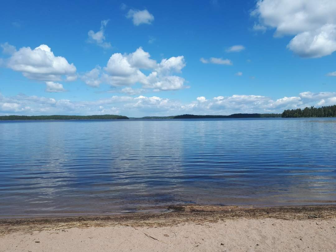 Sammonlahden uimarannalta (hiekkaranta) kuva Saimaalle, jossa kaukana näkyy saaria. Sininen taivas.